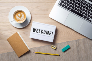 A notecard that says “welcome” next to a cup of coffee and a laptop
